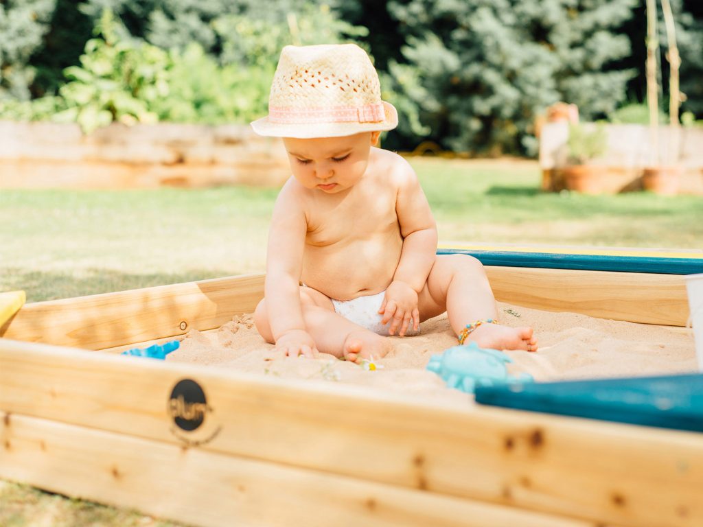 baby playing in the Plum Store-It Wooden Sandpit 