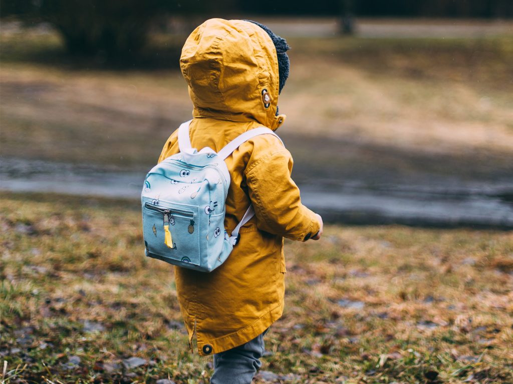 Toddler with backpack and coat walking outside