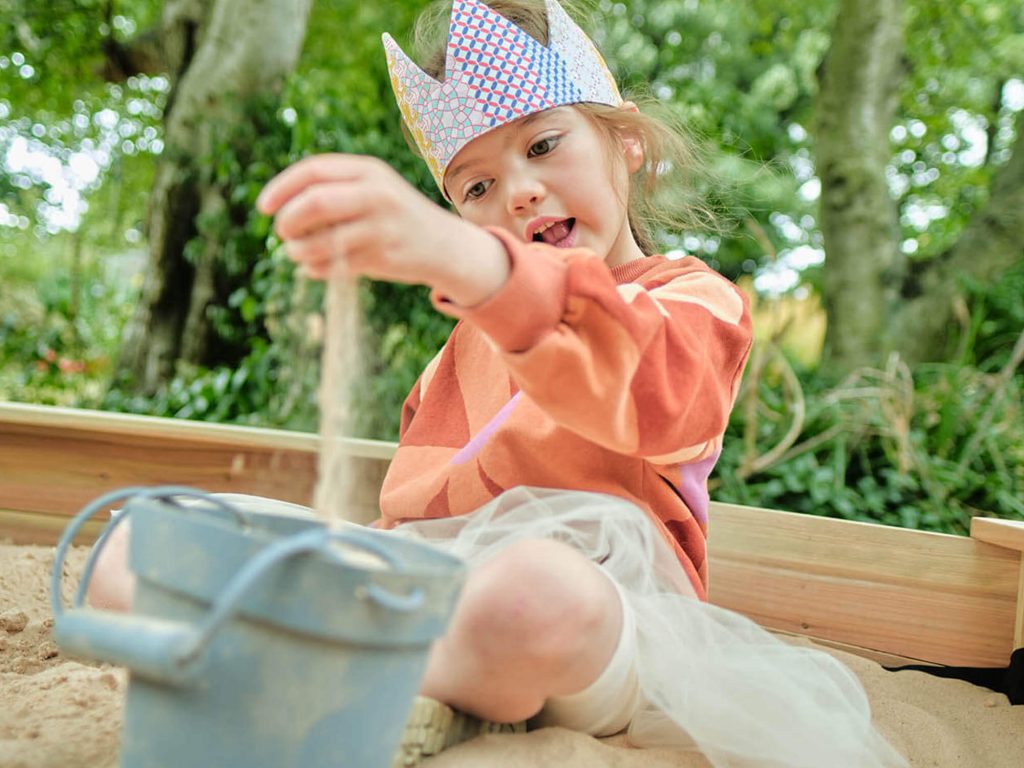 Child playing in sandpit with crown on 